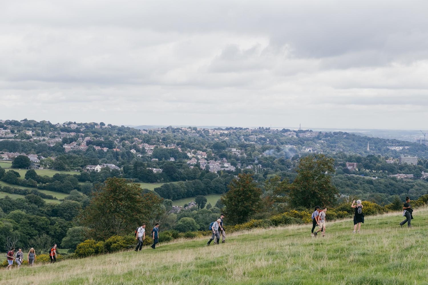 A group of ramblers are walking up a grassy hill. In the background you can see Sheffield city centre.